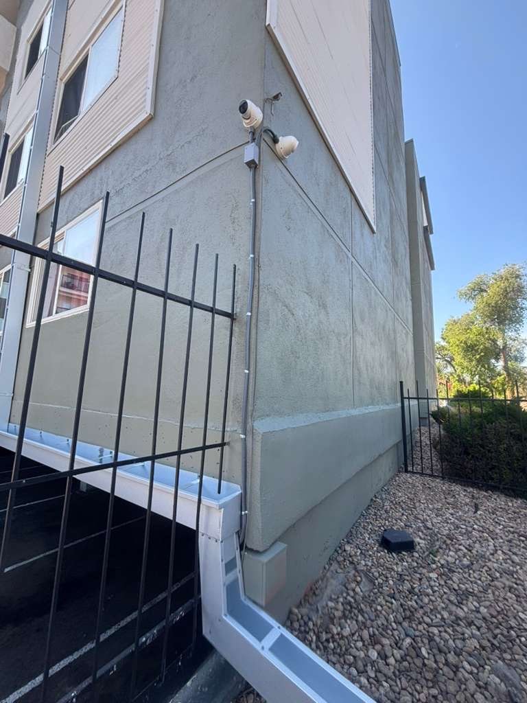 Two cameras and a junction box on the corner of an apartment building with surface conduit