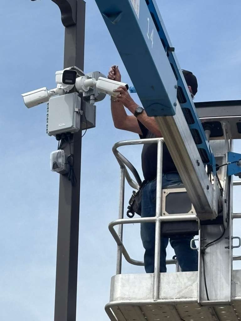 Technician in a lift basket fixing a camera and enclosure to a parking-lot light pole