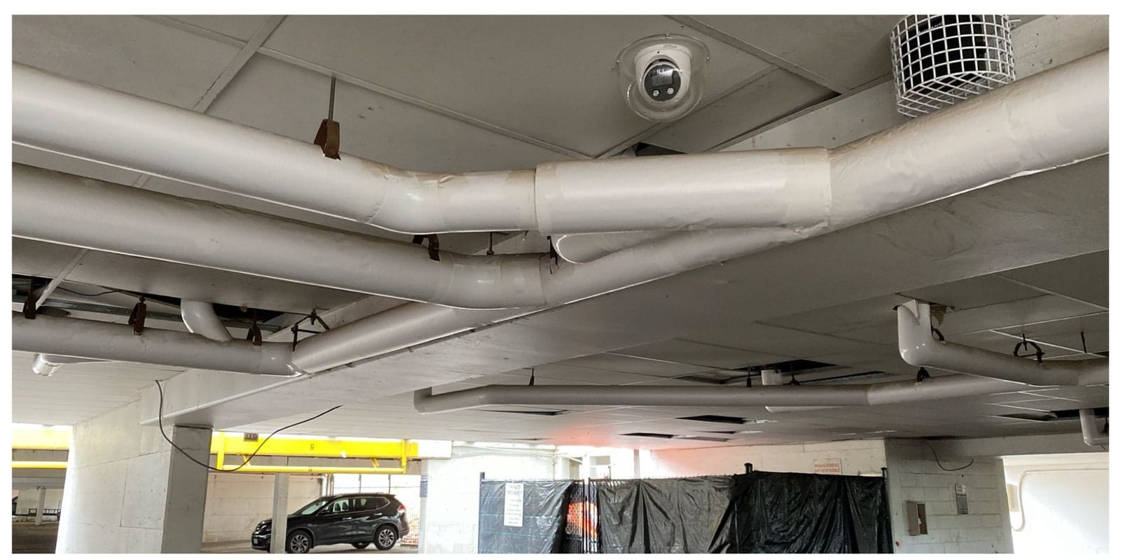 Dome camera on a garage ceiling among sprinkler and drain pipe runs