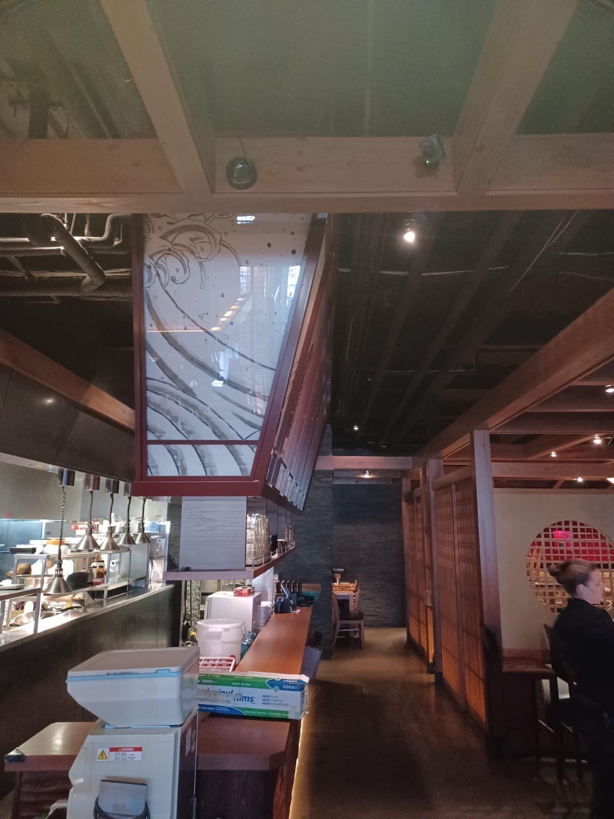 Black security camera integrated into the modern interior lighting and beam structure of a Denver sushi bar