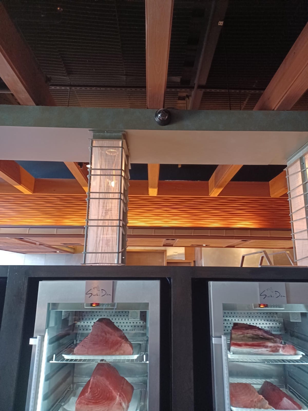 Disguised black dome security camera installed on dark wood architectural beams at Sushi Den Denver