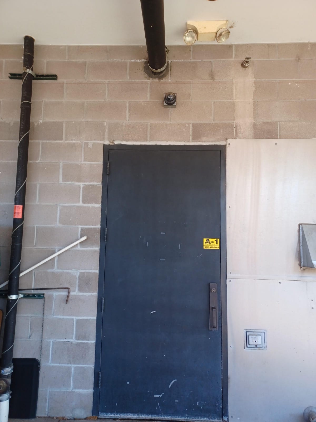 Weatherproof commercial security camera monitoring a steel service exit door at a Denver business