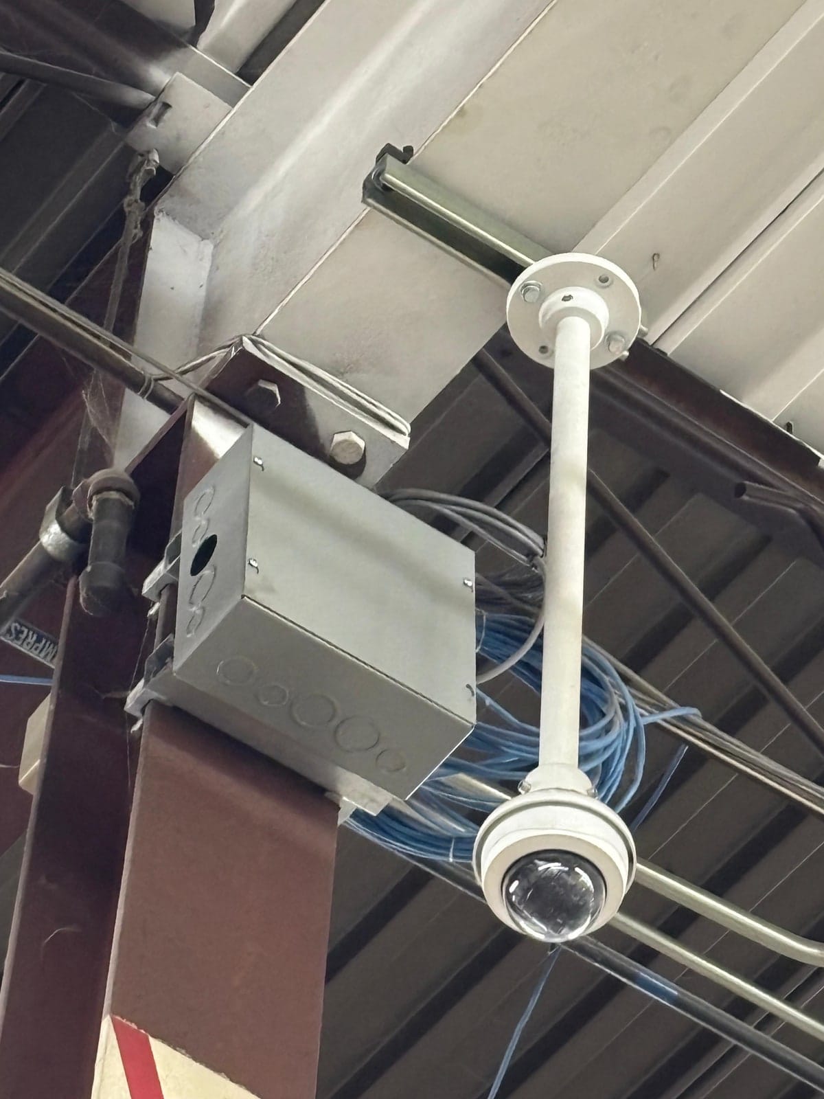 Ceiling camera on a pendant arm beside a junction box with the cable bundle dressed behind it