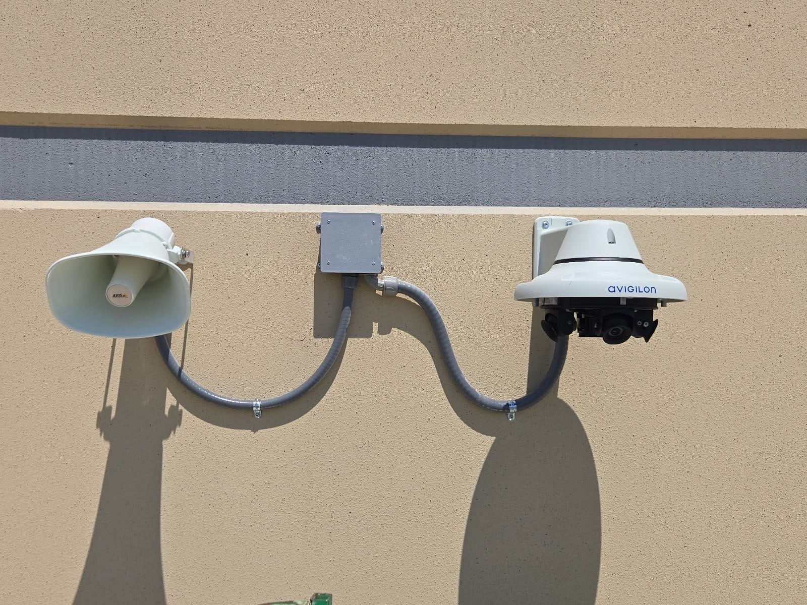 Avigilon multi-sensor camera and outdoor horn speaker joined by liquid-tight conduit on a warehouse wall