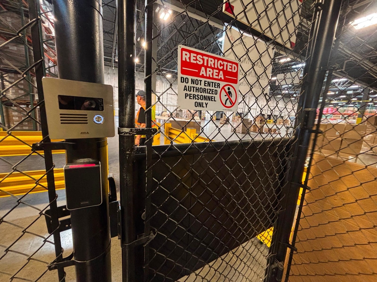 Axis video intercom and Avigilon card reader mounted on the chain-link gate of a restricted warehouse area